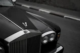 Close-up of a luxury car's polished grille with a blurred Quebec landmark in background.