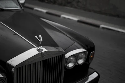 Close-up of a luxury car's polished grille with a blurred Quebec landmark in background.