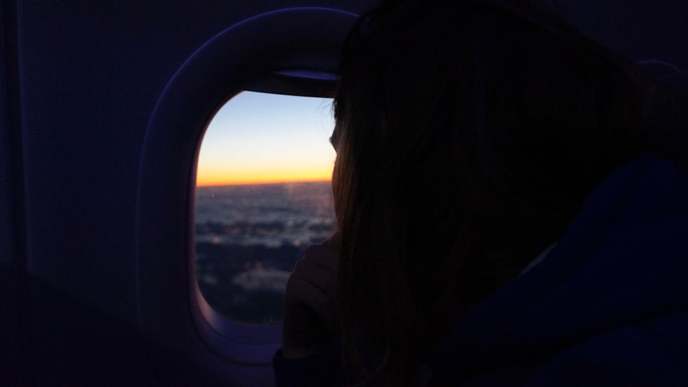 a woman looking out an airplane window at the sunset