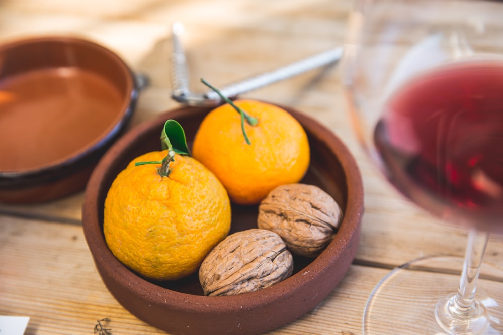 two oranges and two nuts on round brown clay bowl