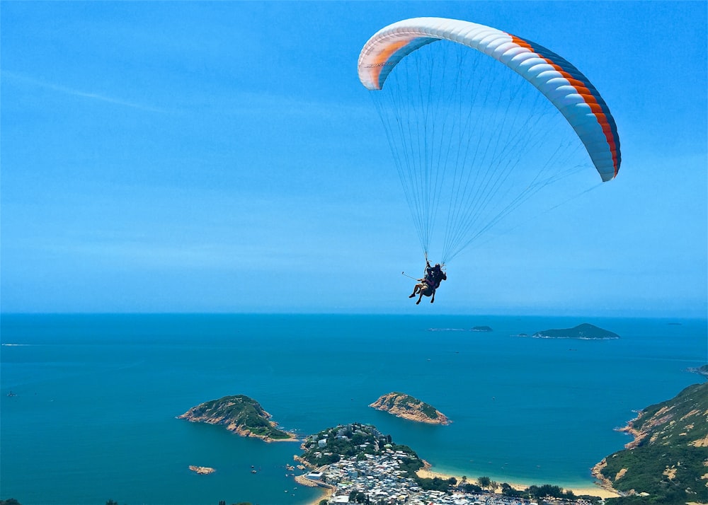 person parachuting over green leaf trees and body of water during daytime