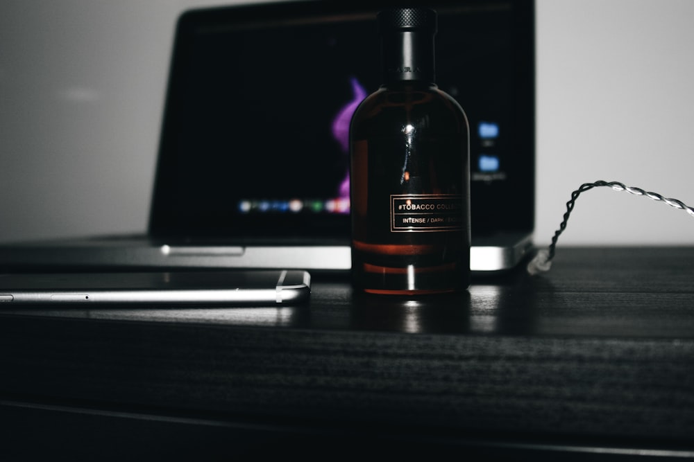 black glass bottle beside smartphone and laptop