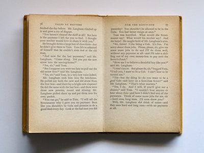 An open book is displayed showing two pages filled with text. The left page is numbered 76 and the right page 77. The text appears to be part of a story titled 'Tales at Bedtime'. The pages have a slightly aged appearance, with yellowing paper and dark text. The book is lying on a flat surface, and its cover is visible along the left edge.