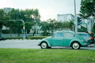 teal Volkswagen beetle parked on gray concrete road during daytime