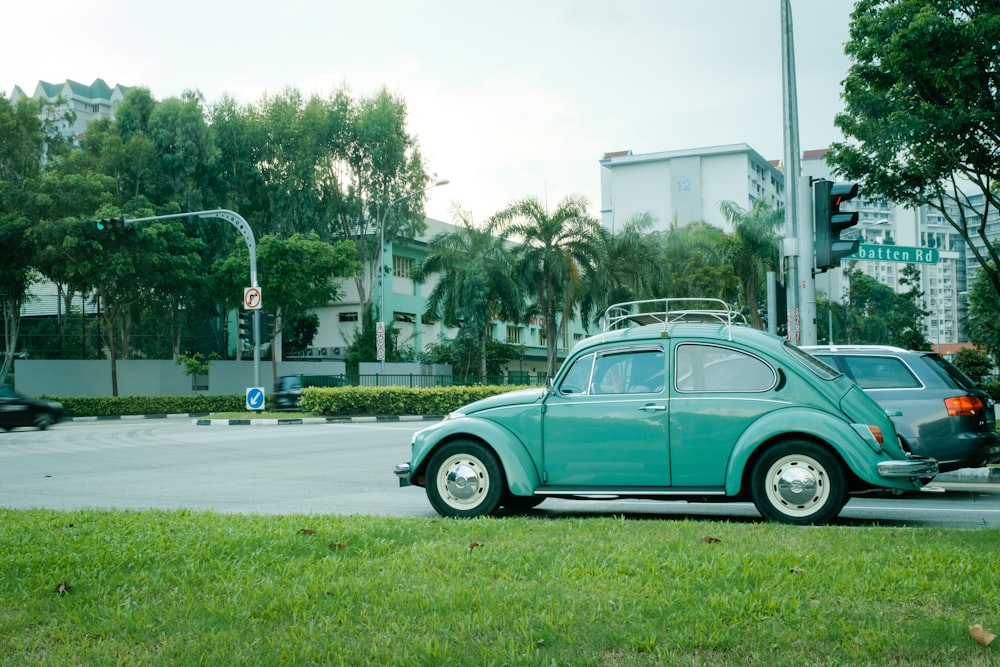 teal Volkswagen beetle parked on gray concrete road during daytime