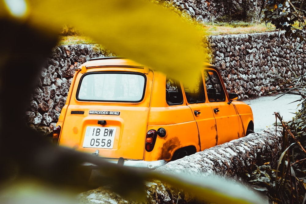 Coche amarillo cerca de la pared de piedra durante el día