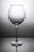 A clear wine glass with a tall stem is centered against a gradient gray background, casting a subtle reflection on the surface below.