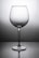 A clear wine glass with a tall stem is centered against a gradient gray background, casting a subtle reflection on the surface below.