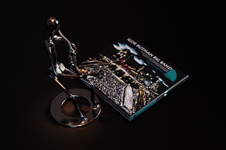 A sleek metallic sculpture of a person playing a saxophone is positioned beside a CD case featuring album art for 'Igor Butman Big Band.' The setting is dark, highlighting the reflective surface of the sculpture and the vibrant colors of the CD cover art.
