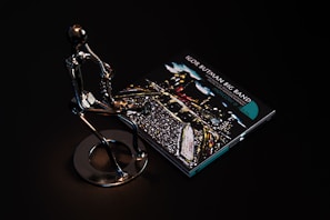 A sleek metallic sculpture of a person playing a saxophone is positioned beside a CD case featuring album art for 'Igor Butman Big Band.' The setting is dark, highlighting the reflective surface of the sculpture and the vibrant colors of the CD cover art.
