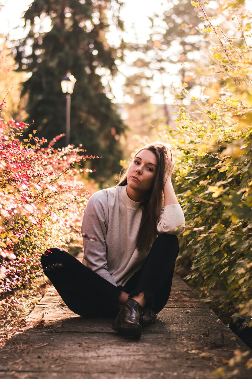 woman sitting on concrete pavement beside shrub during daytime