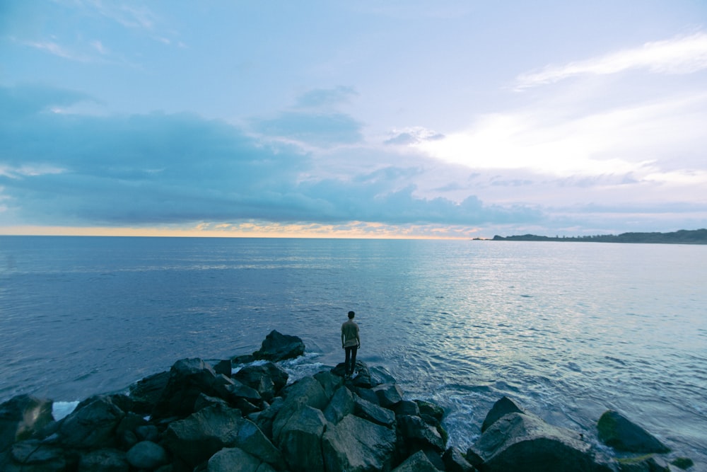 man standing on rock near seashore during daytime