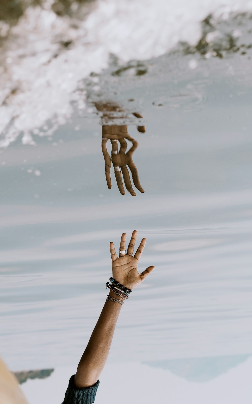 person's hand reaching on water with reflection ]