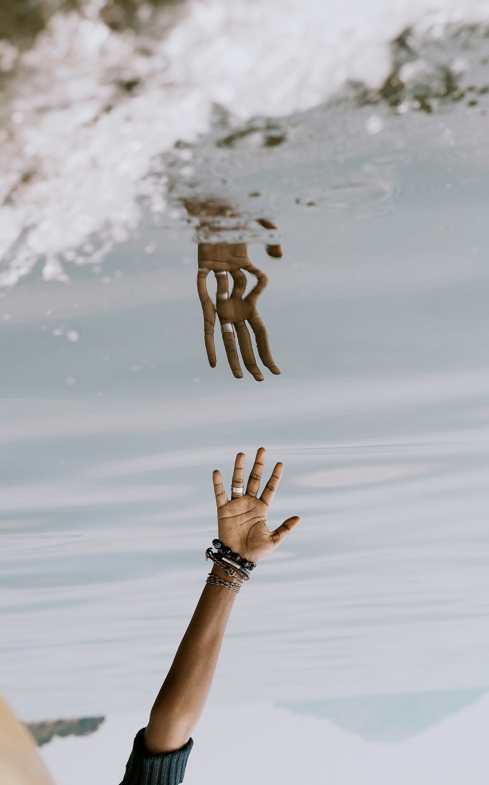 Die Hand der Person greift mit Reflexion auf das Wasser ]