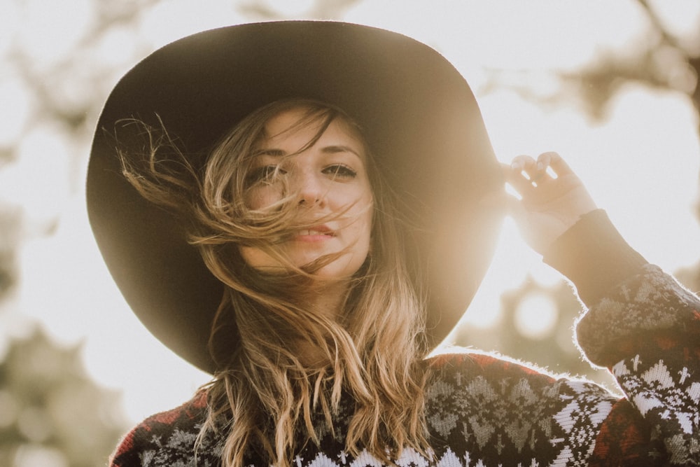 donna che tocca il suo cappello durante il giorno nella fotografia a fuoco superficiale