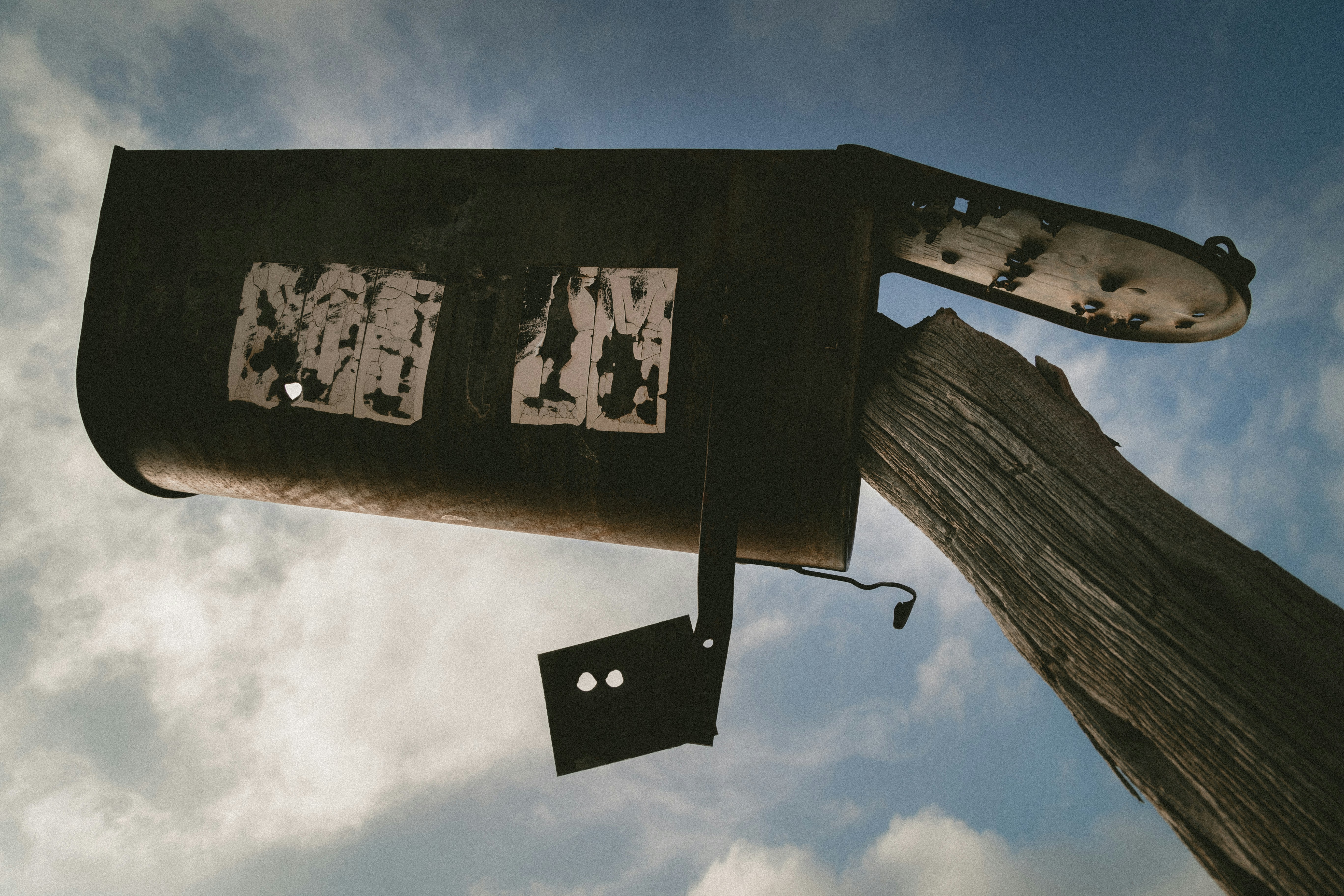 An upside-down rusted old mailbox shoved onto a pole, looking up at it from the ground