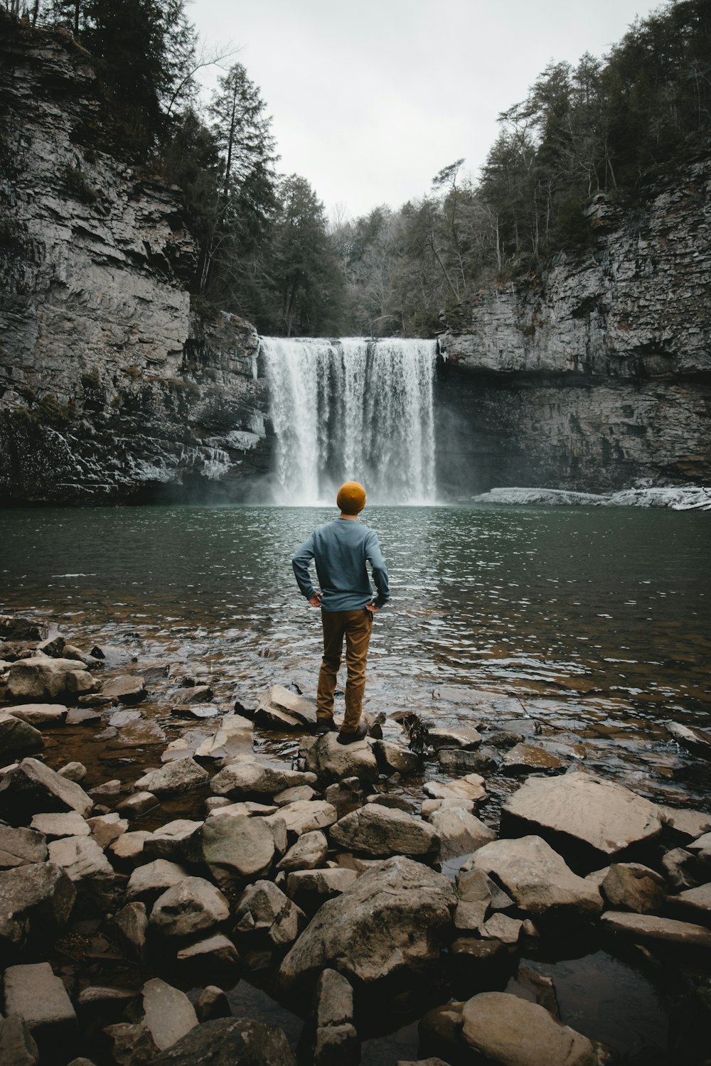 Hombre de pie sobre piedra marrón frente a cascadas