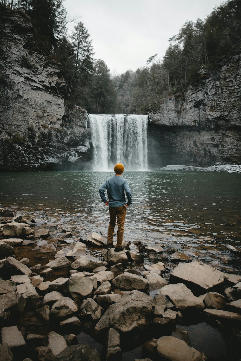 homme debout sur la pierre brune face aux chutes d’eau