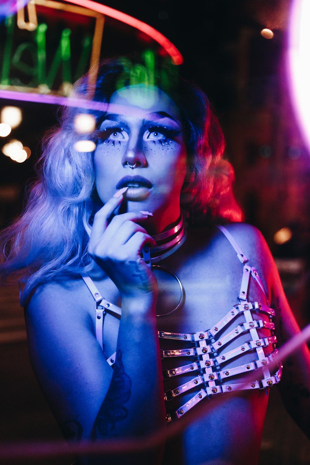 a woman in a bra top smoking a cigarette in front of a neon sign