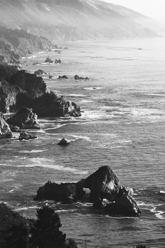 gray scale aerial photography of water surround by rock formaitions in Big Sur United States