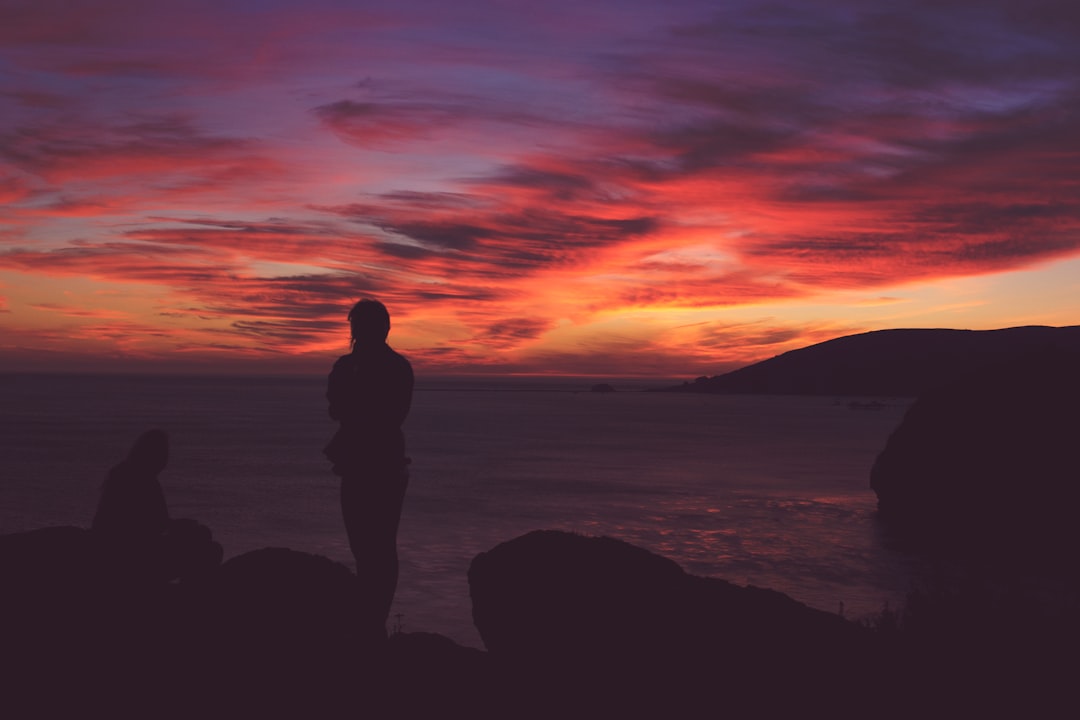 silhouette photo of person standing near sea during golden hour