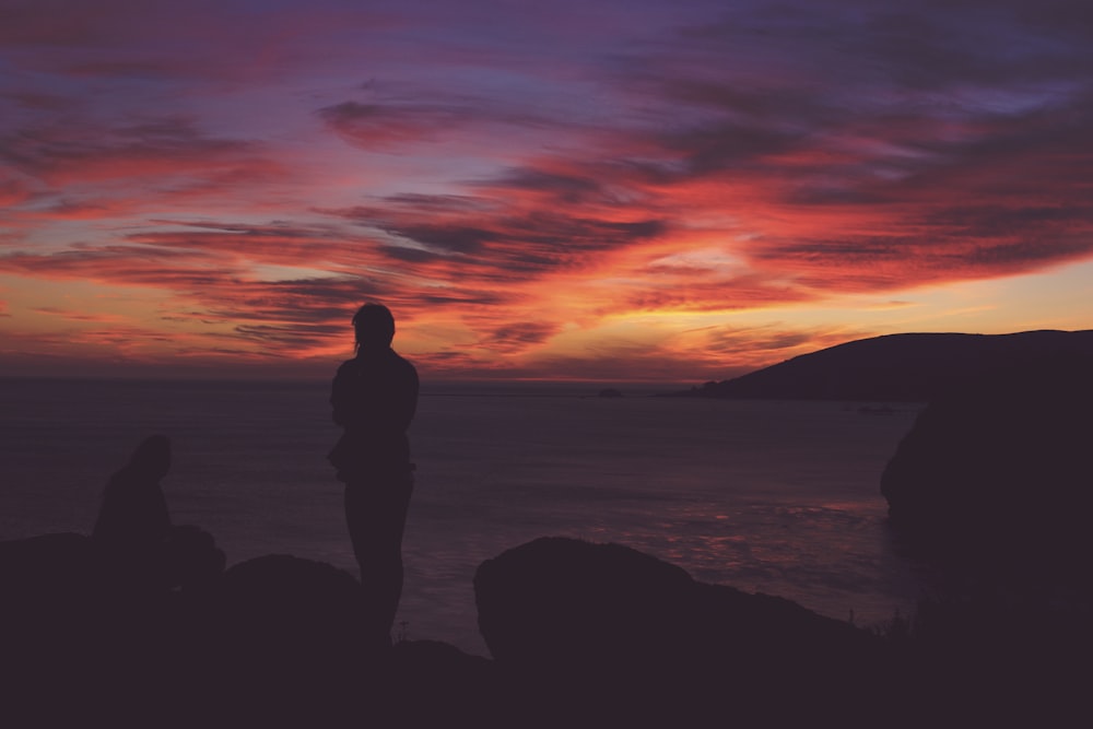 silhouette photo of person standing near sea during golden hour