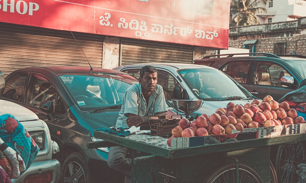 昼間、駐車中の車の近くでリンゴを売っている男性