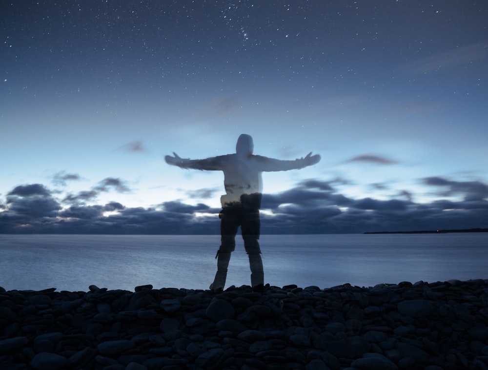 edited photo of person standing on rocks near sea during nighttime