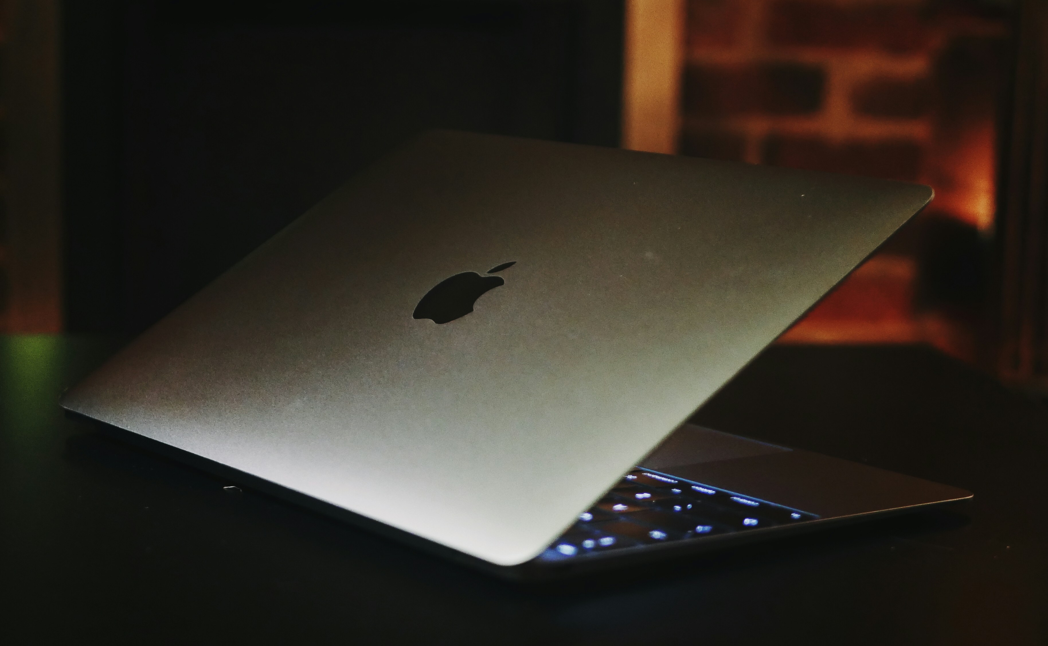 Silver MacBook Pro laptop open on dark desk with glowing keyboard