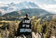 person standing on mountain peak with black land of the dreamer-printed cape on his back