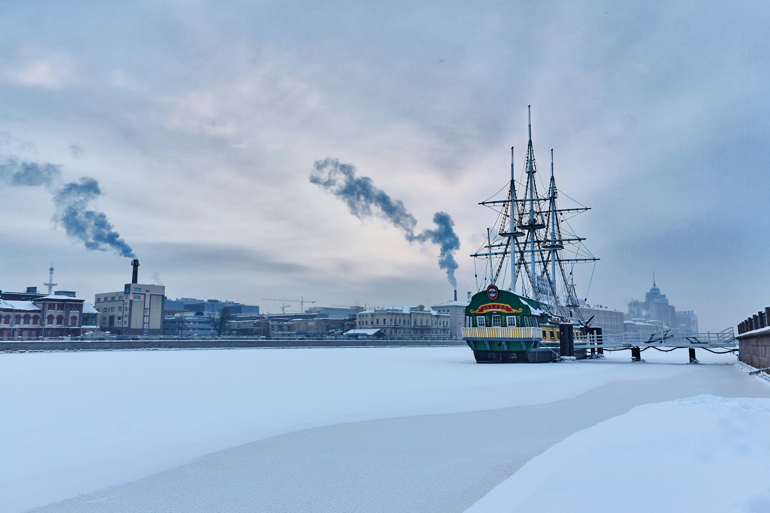 green train in winter with industrial smokestack emitting smoke in background
