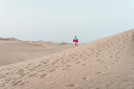 photo of person walking on desert holding red box in Canary Islands Spain