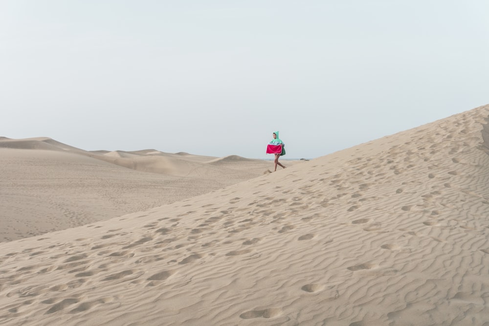 photo of person walking on desert holding red box