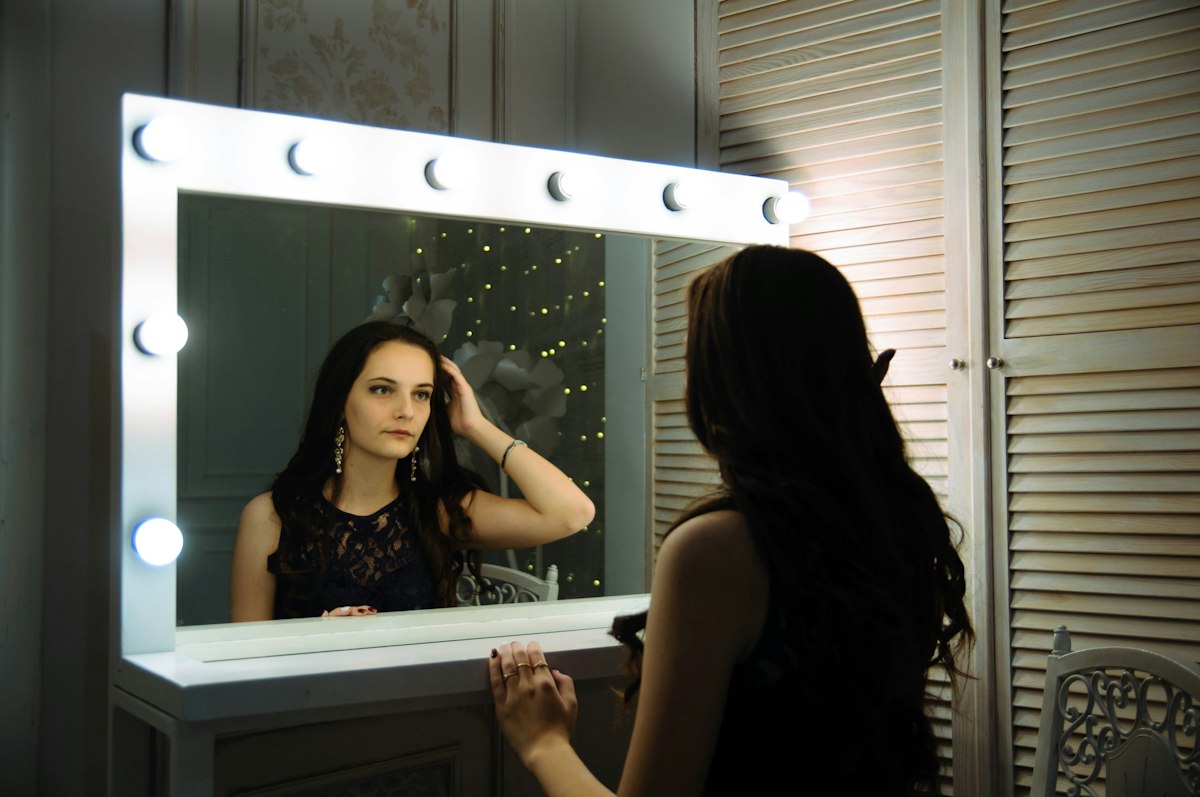 Woman sitting in front of a lighted vanity mirror
