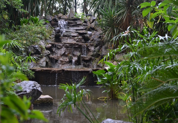 A serene garden scene showcasing a handcrafted FRP planter beside a gentle cascading waterfall.