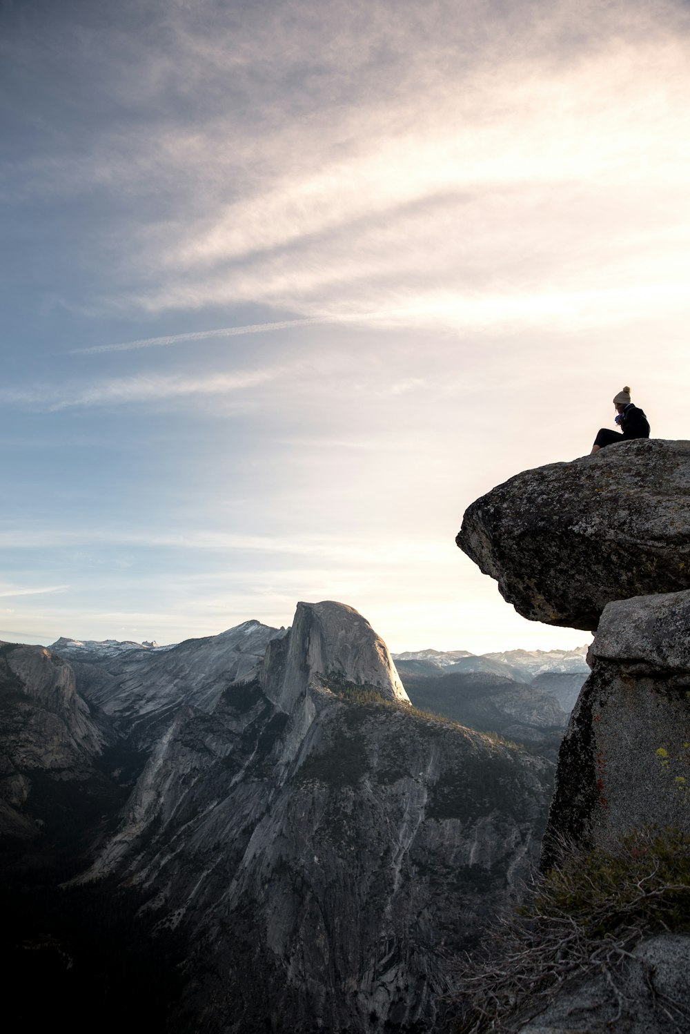 person sitting on gray rock cliff at daytime