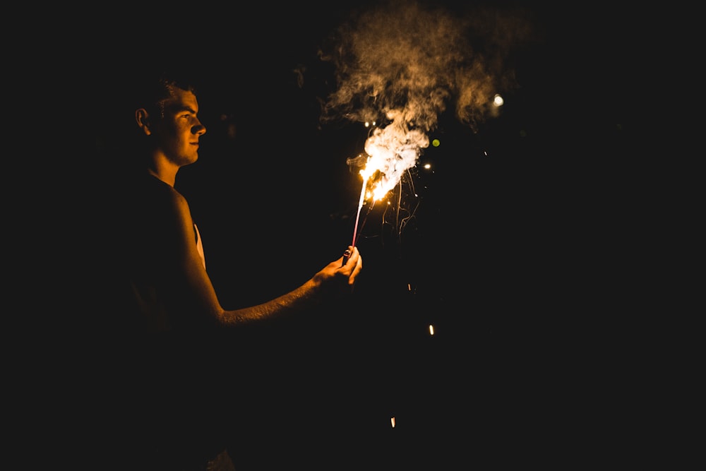 a man holding a lit sparkler in the dark