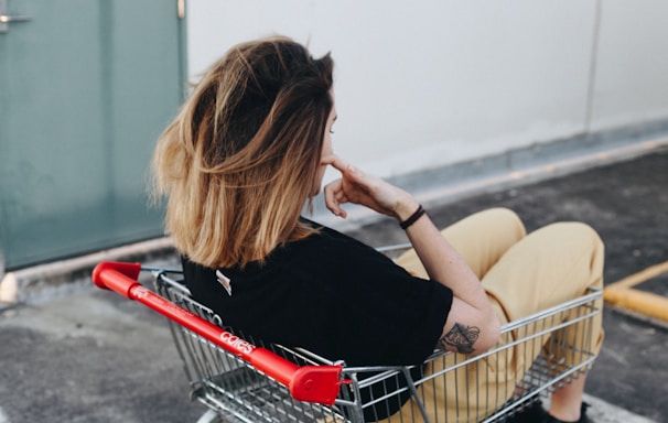 woman sitting on shopping cart near the wall