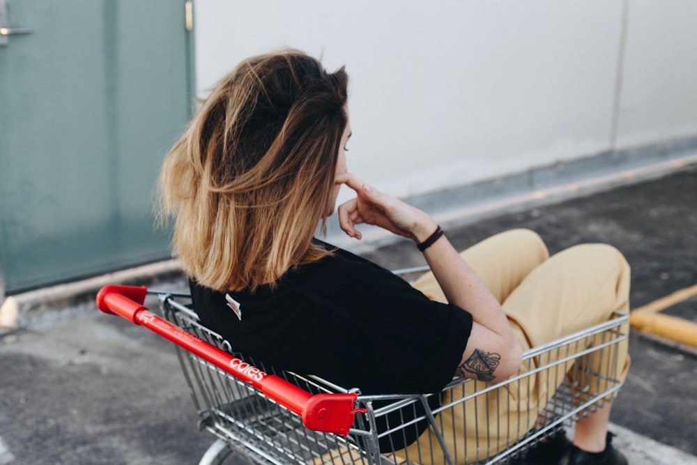 Mujer sentada en el carrito de la compra cerca de la pared