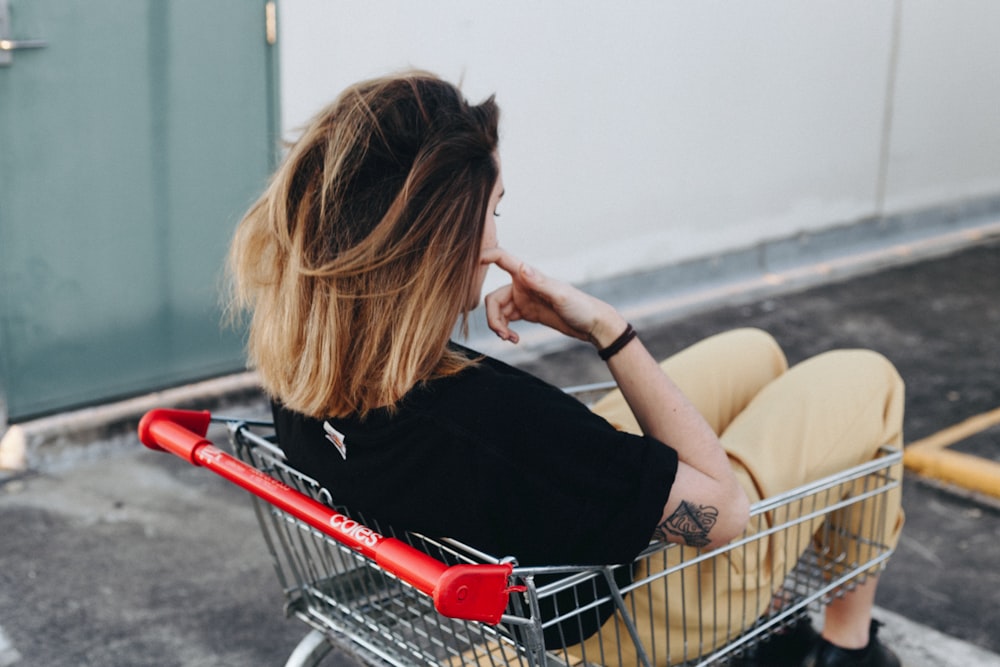 woman sitting on shopping cart near the wall