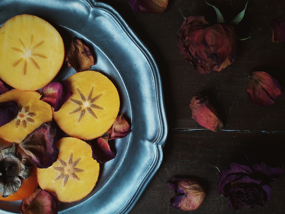 sliced persimmon fruits and withered red roses on gray plate