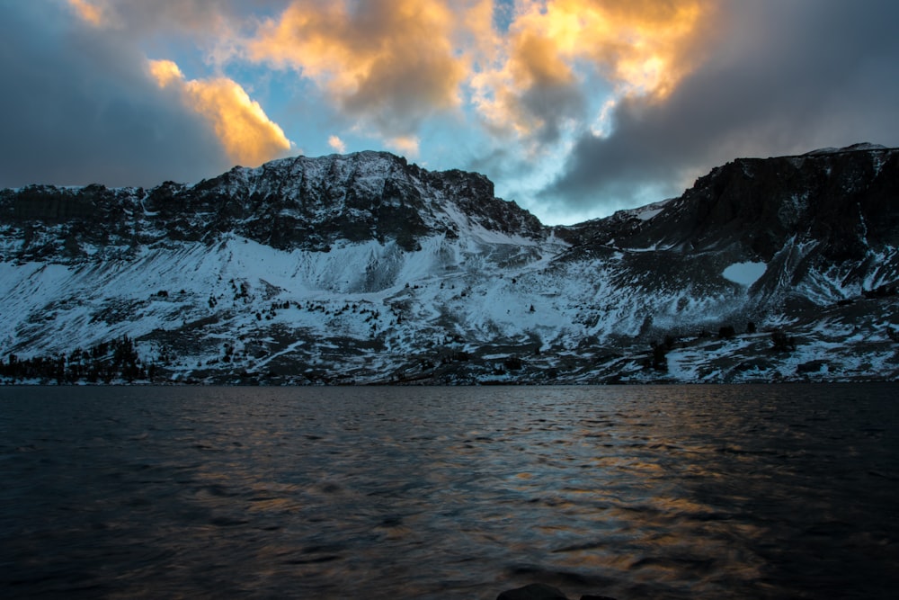 gray mountain covered by snow beside body of water