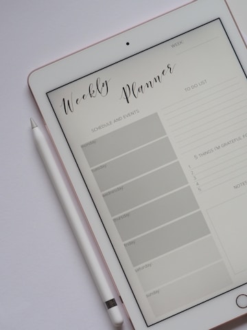 A tablet displaying a digital weekly planner is placed on a light-colored surface. The planner layout includes sections for schedule and events from Monday to Sunday, a to-do list, and a space for notes and gratitude. A stylus rests beside the tablet, suggesting interaction with the planner.