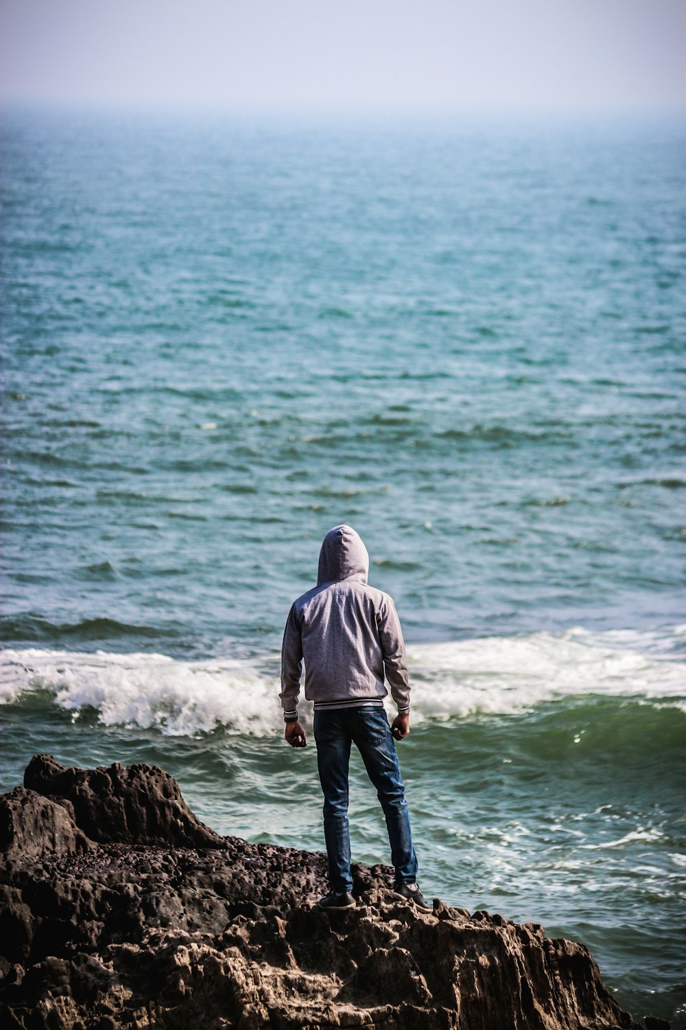 man standing on cliff facing body of water