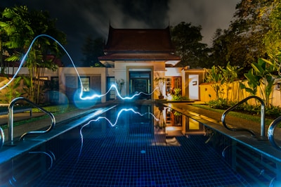 reflection of blue light crossing above pool near house during nighttime