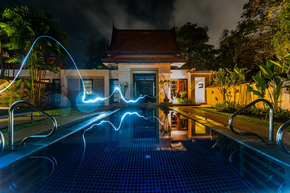 reflejo de la luz azul que cruza por encima de la piscina cerca de la casa durante la noche