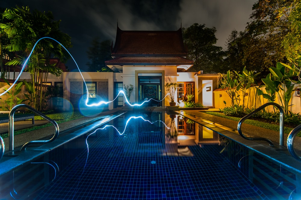 reflection of blue light crossing above pool near house during nighttime