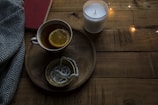 A minimalist wooden tray holding a steaming cup of tea beside a gently flickering candle.