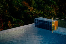 Close-up of a pool edge with soft green lighting and natural wood grain, framed by lush tropical plants.
