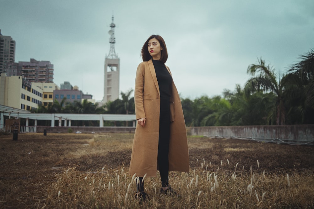 woman wearing brown coat standing on brown grass